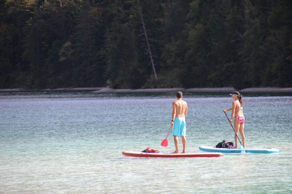 Zwei Personen paddeln auf SUP-Boards auf einem ruhigen Bergsee – Darstellung beliebter Wassersportarten neben dem Awake Board